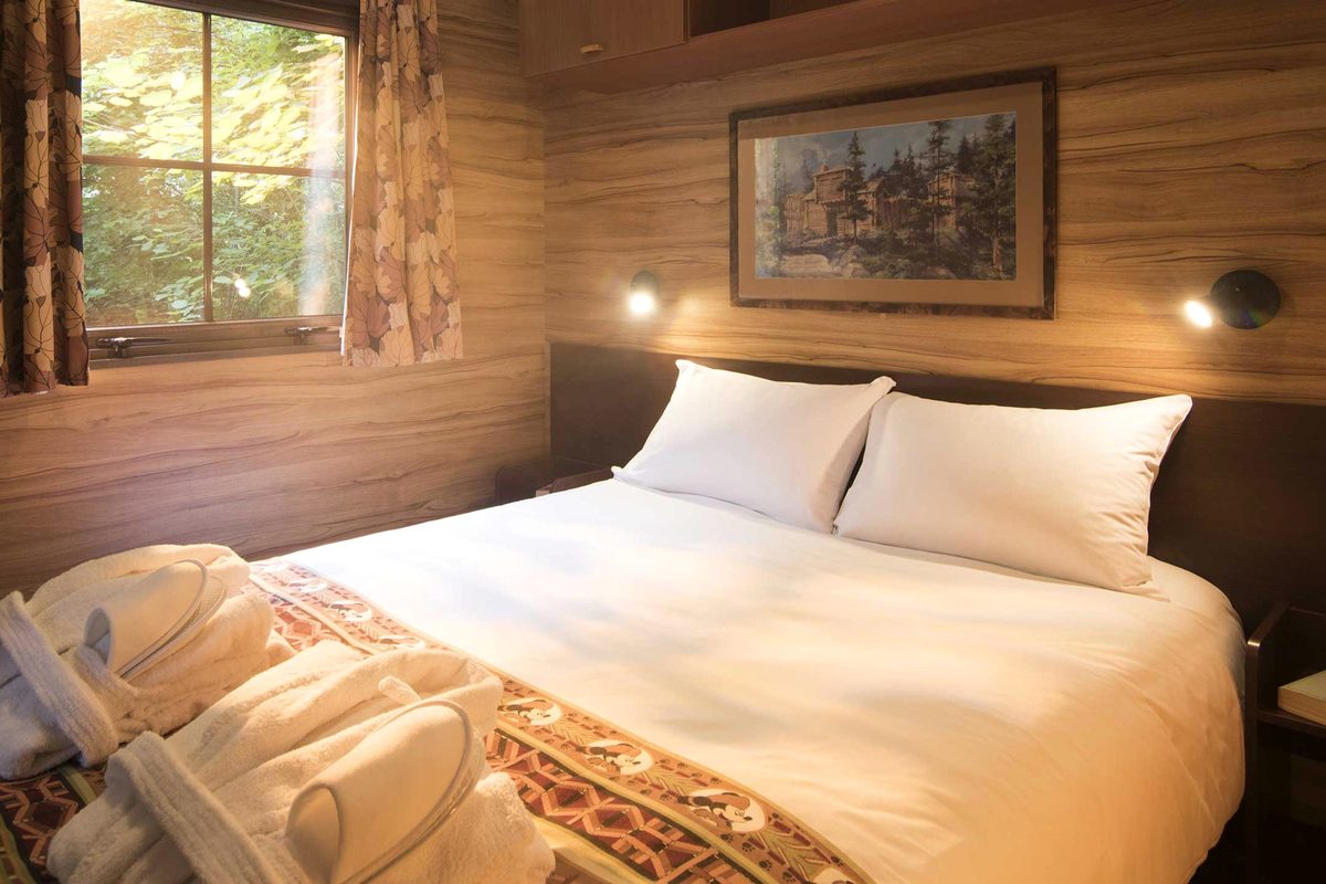 The master bedroom in a Davy Crockett Ranch cabin, a double bed made up in white linen with towels and slippers set out and a framed lodge print above the headboard