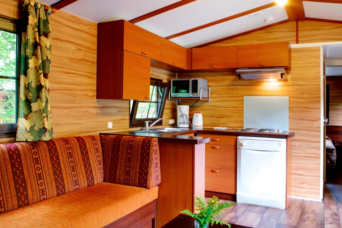 The open-plan living room and kitchen inside a Davy Crockett Ranch cabin, a sofa and dining area with a kitchen along one wall holding a hob, microwave, dishwasher and coffee machine