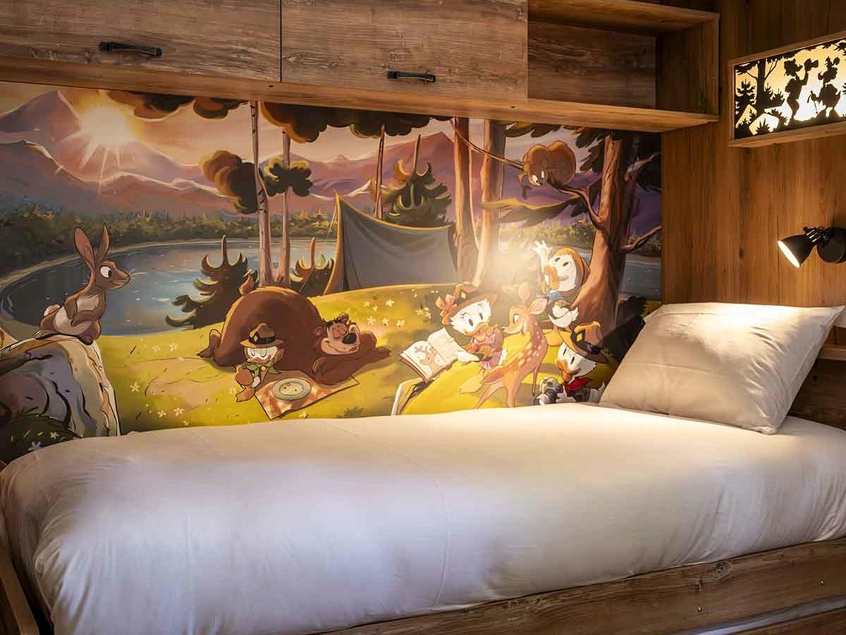 A child's bed in a new Davy Crockett Ranch cabin, beneath a mural of the Junior Woodchucks camping by a lake