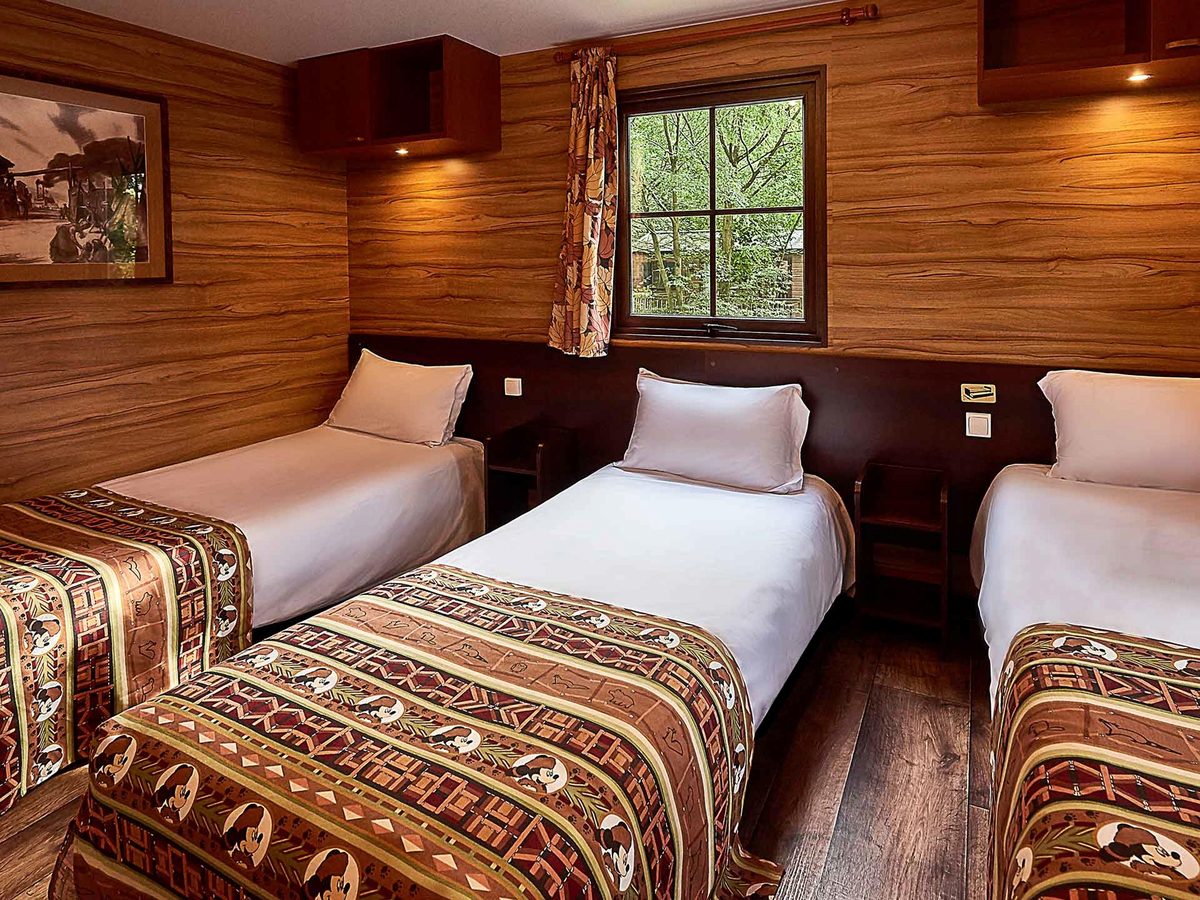 The second bedroom of a new Davy Crockett Ranch cabin, three single beds in warm wood panelling with woodland-patterned covers