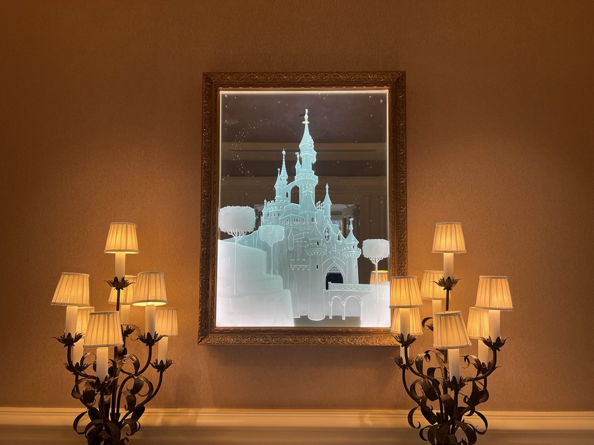 An illuminated etched-glass castle in a gold frame between candelabra lamps in a Disneyland Hotel guest room