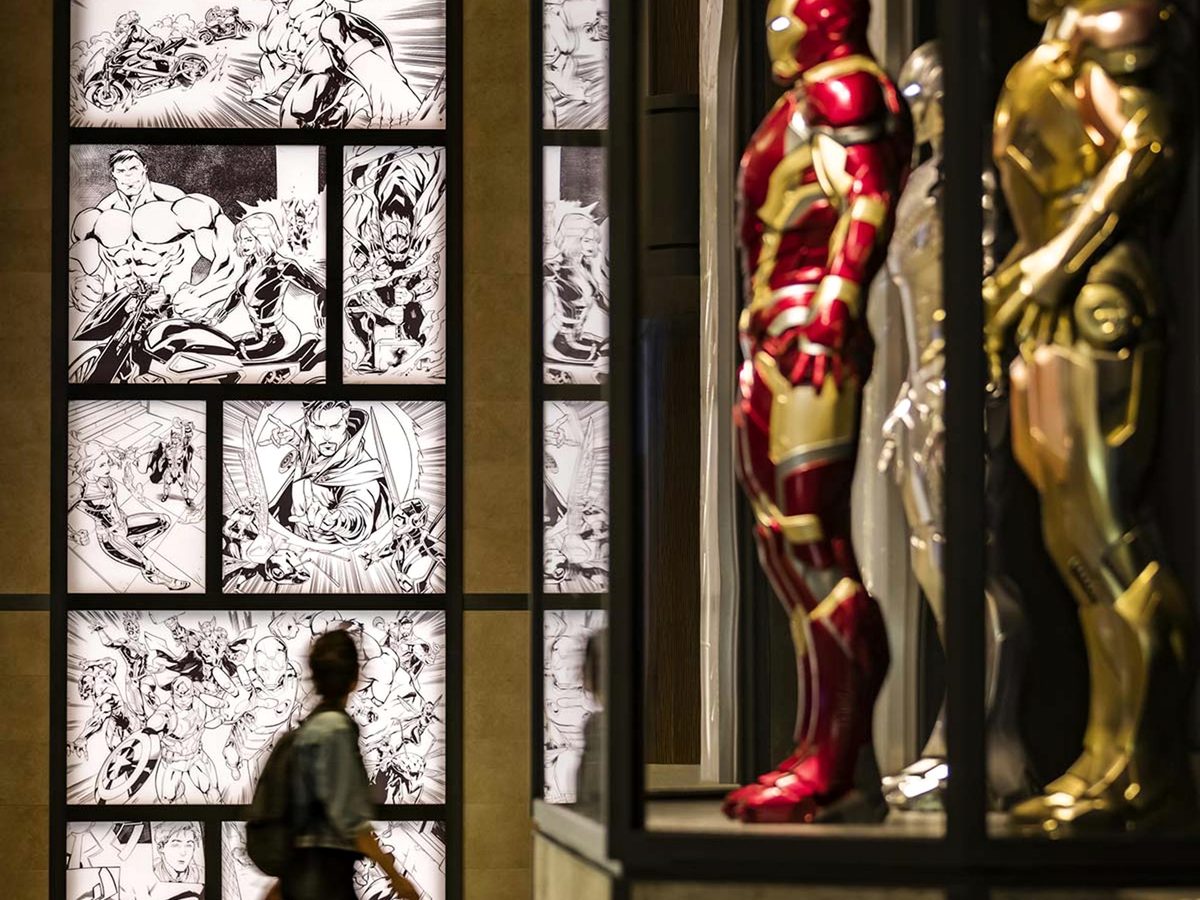 Life-size Iron Man suits in a glass case in the lobby of Disney Hotel New York – The Art of Marvel, with backlit black-and-white comic panels behind