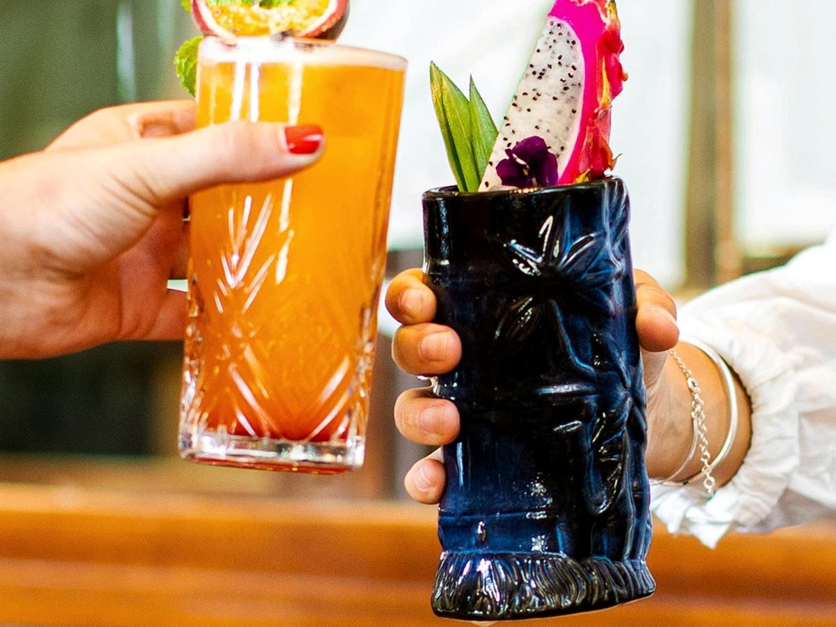 Two cocktails raised at the Captain's Quarters bar at Disney Newport Bay Club, one in a carved tiki mug topped with dragon fruit