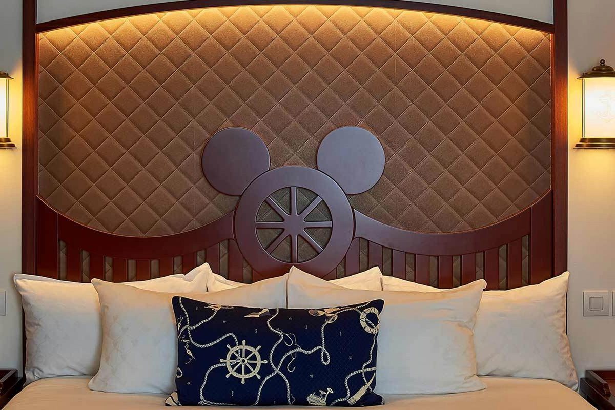 The illuminated Mickey headboard in a Compass Club room, backlit against a quilted panel with a ship-wheel porthole and a rope-patterned cushion below