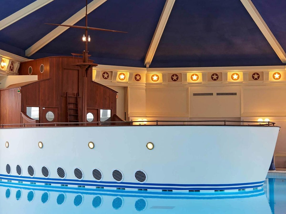 The climb-on ship at the indoor Nantucket Pool at Disney Newport Bay Club, portholes along its white hull beneath a deep-blue canopy ceiling