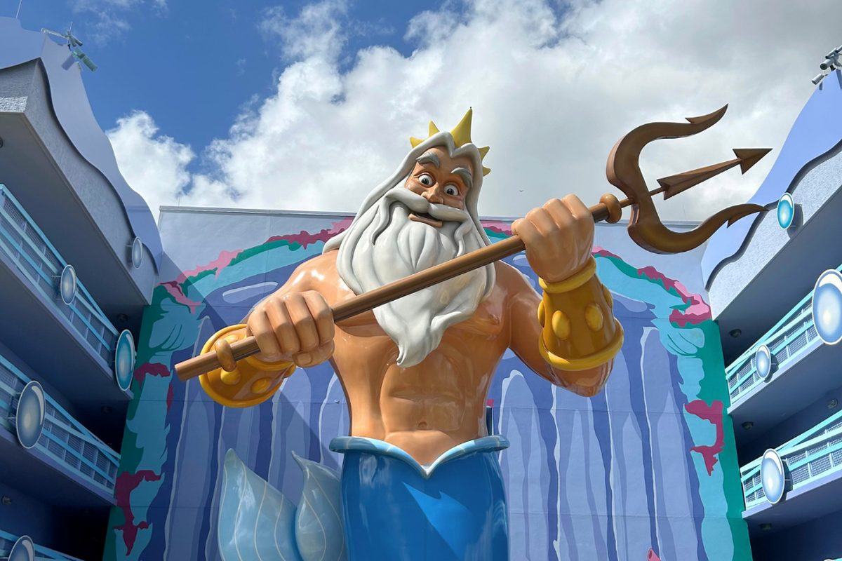 A giant King Triton statue on the wall of the Little Mermaid wing at Disney’s Art of Animation Resort, trident raised against a blue sky.