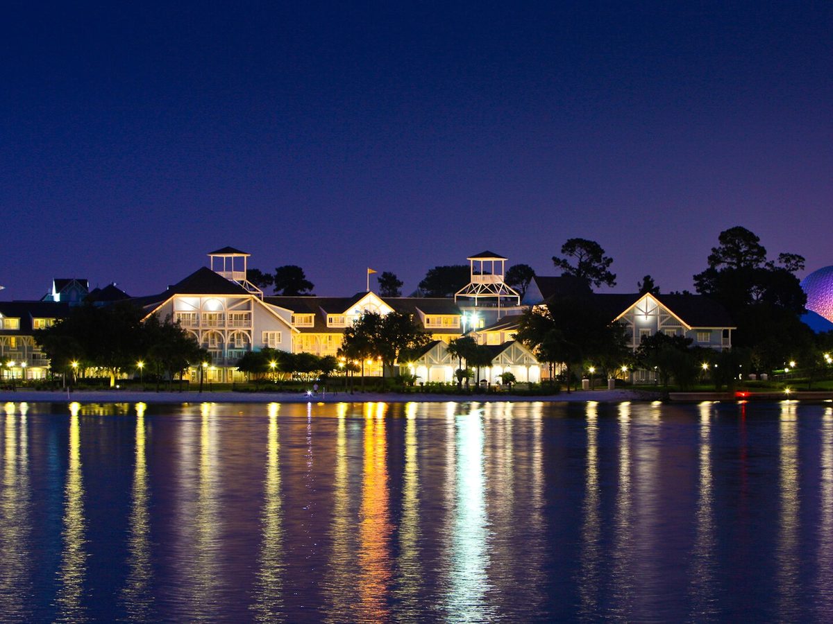 The Beach Club lakefront lit at dusk, its lights reflecting in Crescent Lake with EPCOT's Spaceship Earth glowing beyond
