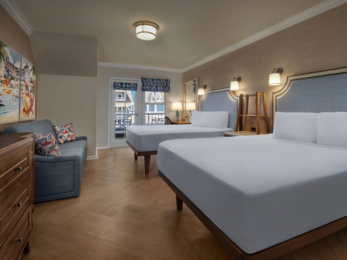 A refreshed Beach Club room with two queen beds, pale-blue leather headboards, a grey sofa and seaside artwork