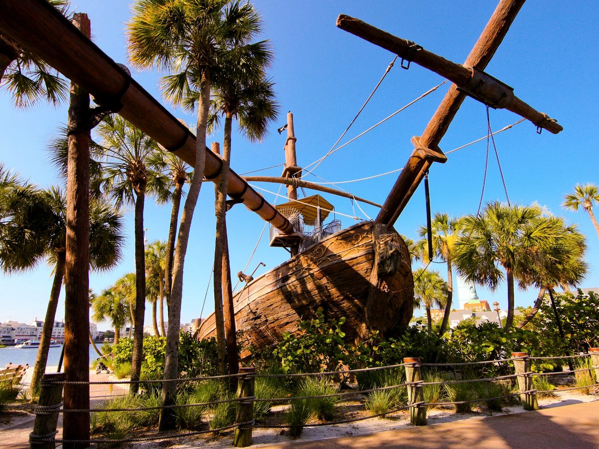 The grounded wooden shipwreck at Stormalong Bay among palm trees, its masts against a clear sky
