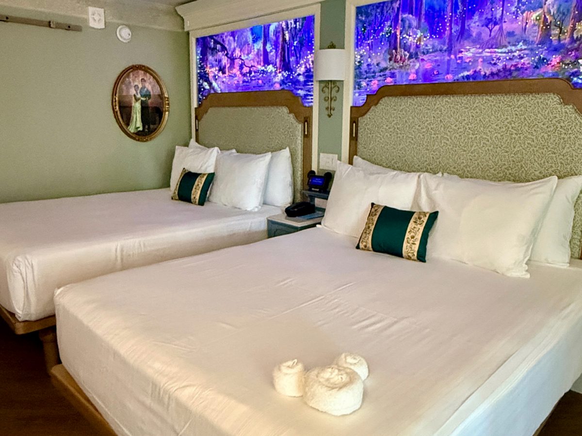 A Royal Guest Room at Disney's Port Orleans Riverside, two queen beds with glowing bayou murals above the headboards and a portrait of Tiana and Naveen on the wall