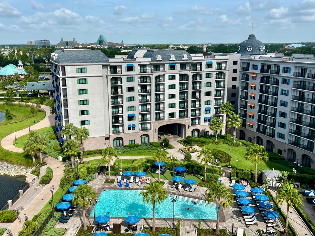 The pool courtyard at Disney's Riviera Resort seen from an upper floor, blue parasols around the water and Skyliner gondolas passing on the left