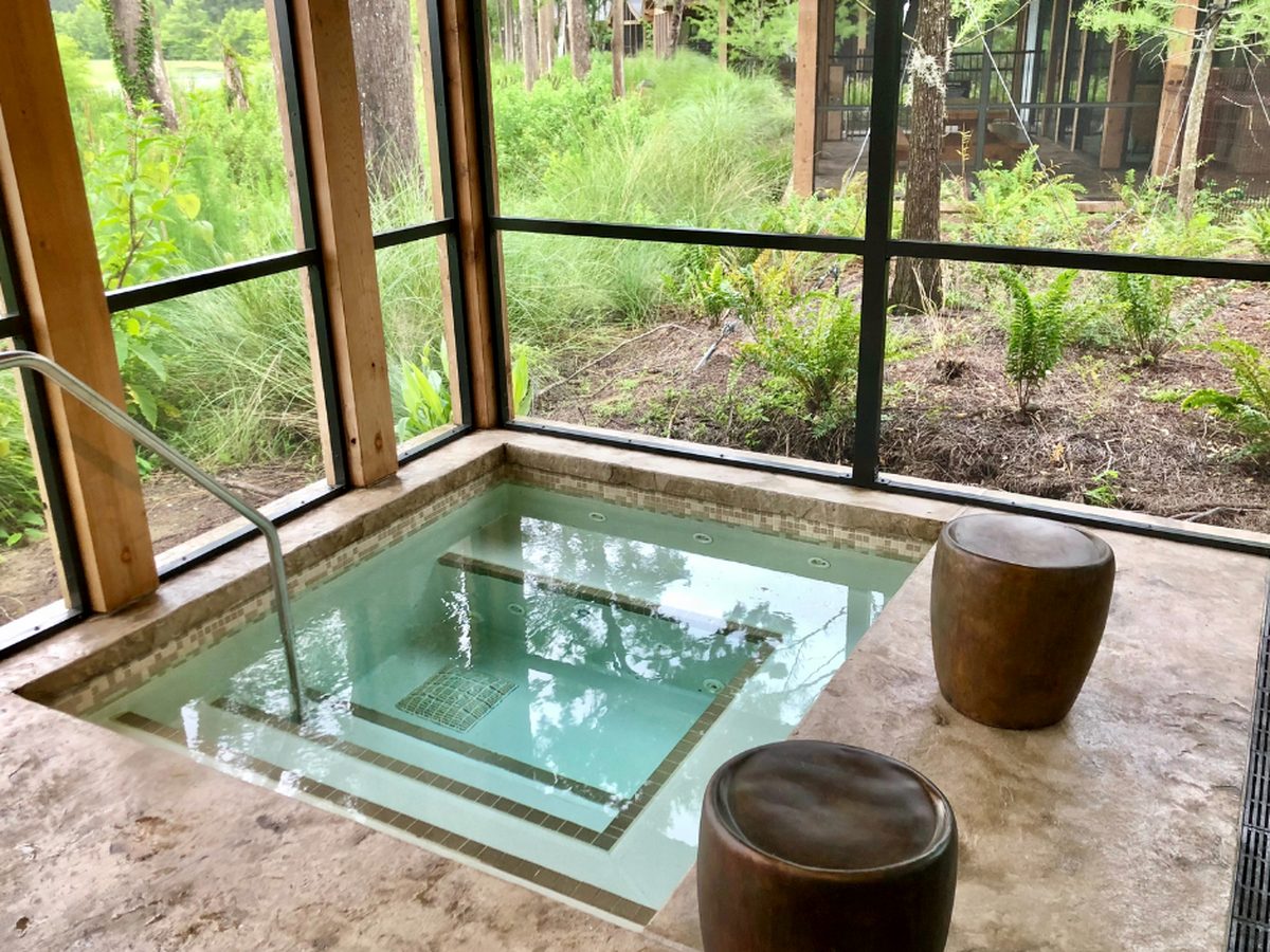 The built-in hot tub sunk into the stone floor of a Cascade Cabin's screened porch at Disney's Wilderness Lodge, looking out at woodland and a neighbouring cabin
