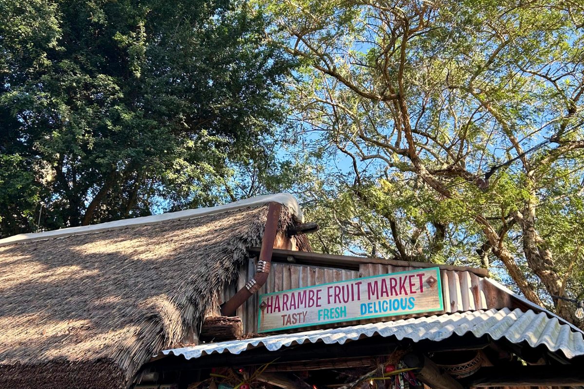 The Harambe Fruit Market sign on the thatched stand in the Africa area of Animal Kingdom, trees behind