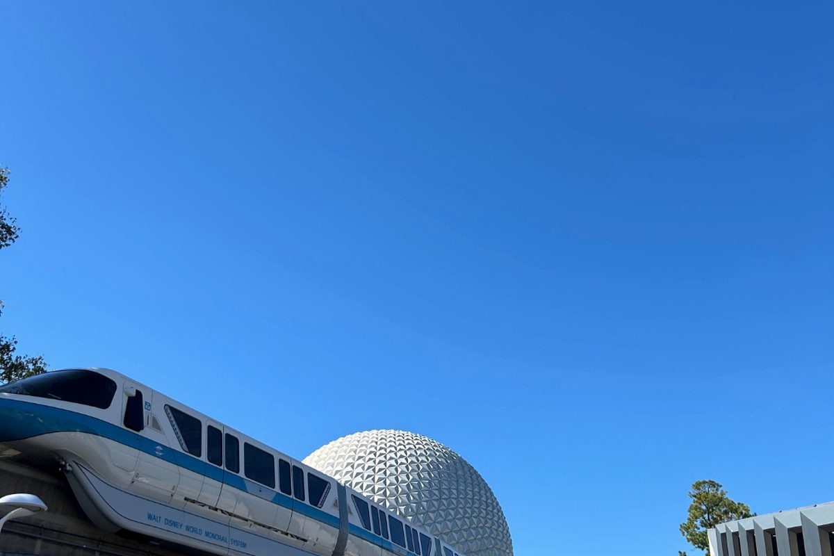 A Walt Disney World monorail passing in front of the Spaceship Earth geosphere under a clear blue sky at EPCOT