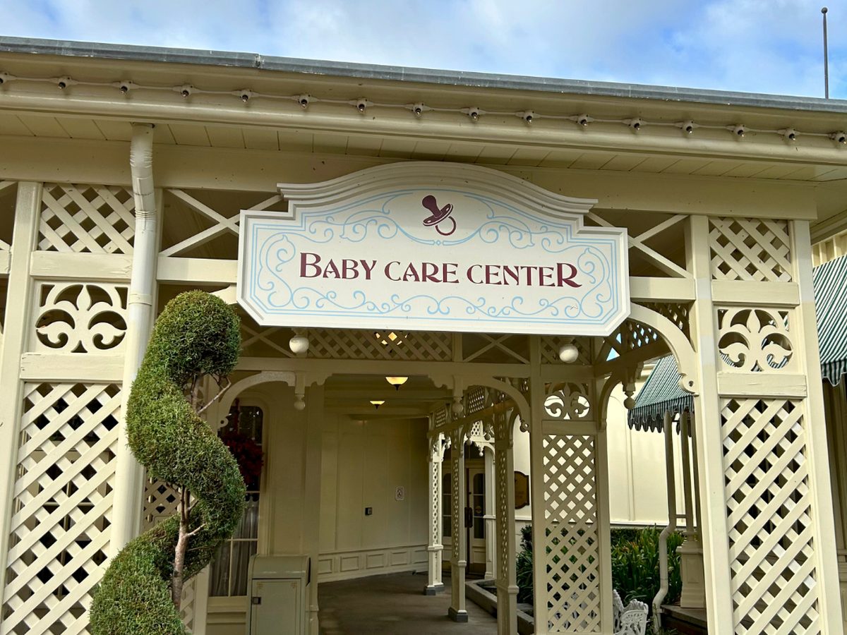 The cream lattice porch and sign of the Baby Care Center near the top of Main Street at Magic Kingdom, a spiral topiary beside the entrance