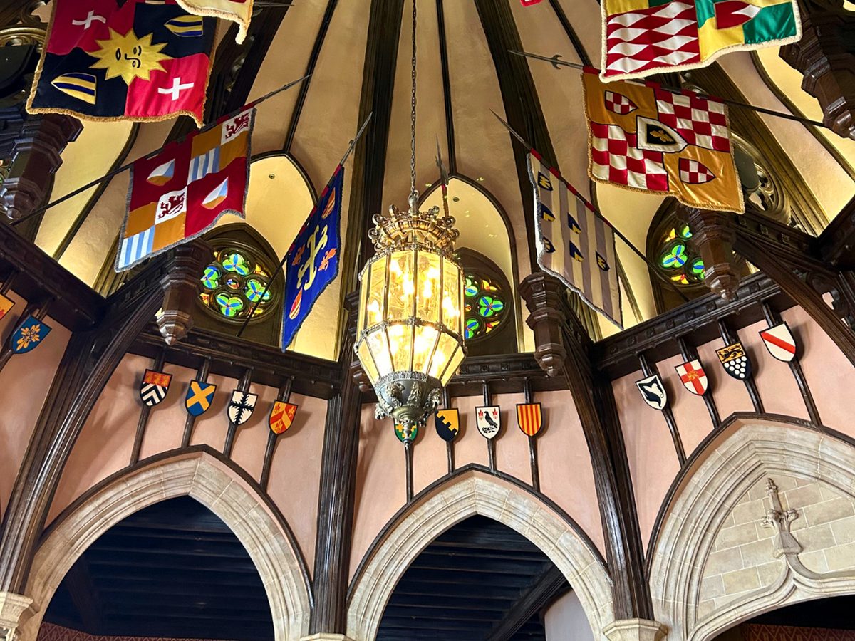 The vaulted dining hall inside Cinderella's Royal Table at Magic Kingdom, heraldic banners, coats of arms, stained glass and a hanging lantern
