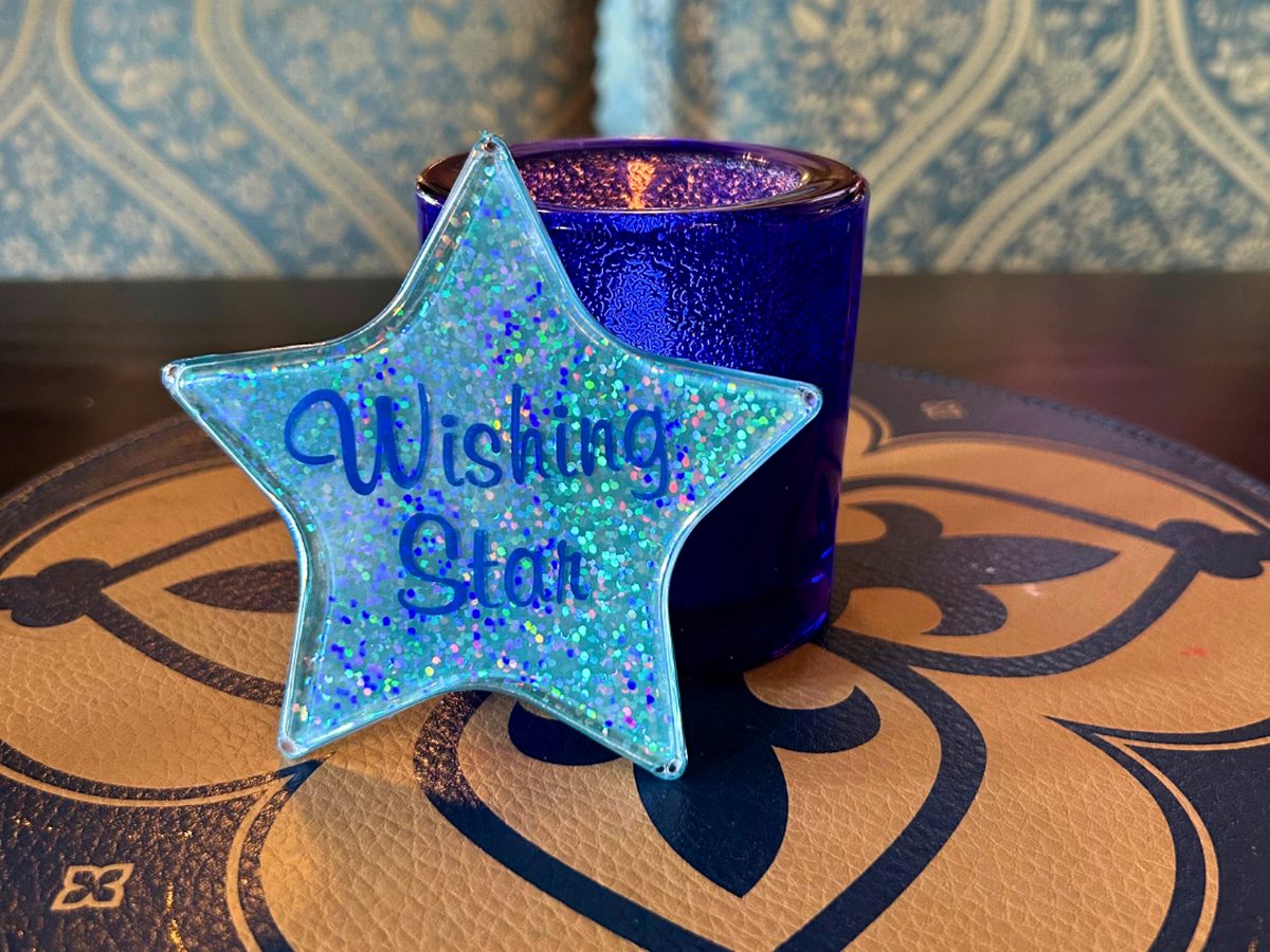 A glittery light-up wishing star from Cinderella's Royal Table at Magic Kingdom, propped against a blue glass on a heraldic table mat