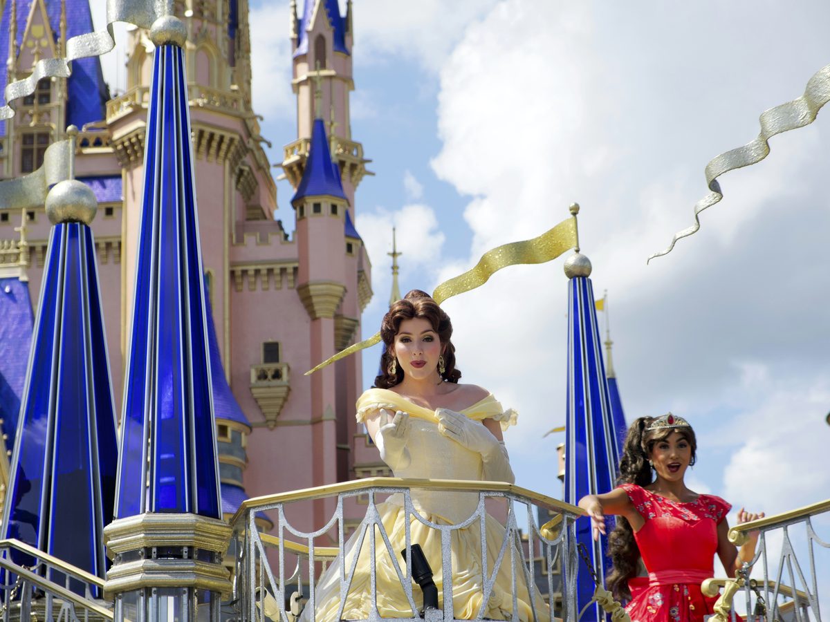 Belle in her yellow gown and another princess waving from a Disney Festival of Fantasy parade float at Magic Kingdom, the spires of Cinderella Castle behind