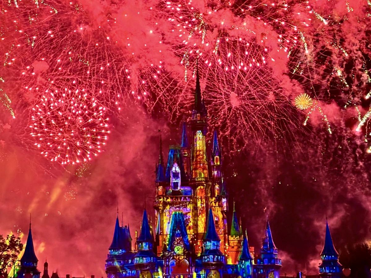 Red fireworks filling the sky over Cinderella Castle at Magic Kingdom, the castle lit in colour during the nighttime show