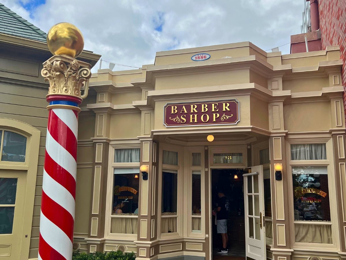 The Harmony Barber Shop entrance on Main Street at Magic Kingdom, a red and white striped barber's pole beside the Barber Shop sign