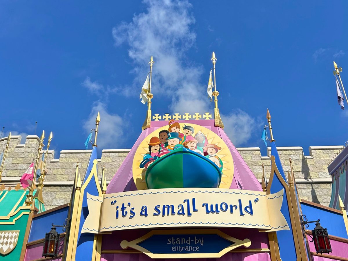 The pastel "it's a small world" facade at Magic Kingdom, the boat-and-children sign over the stand-by entrance against a blue sky