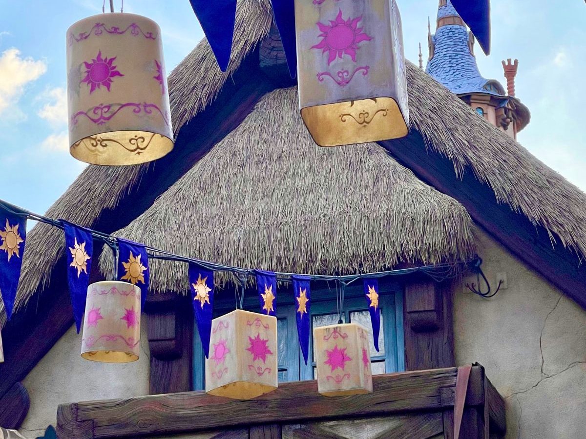 The thatched, lantern-hung Tangled courtyard in Fantasyland at Magic Kingdom, paper lanterns and purple sun banners strung over the building