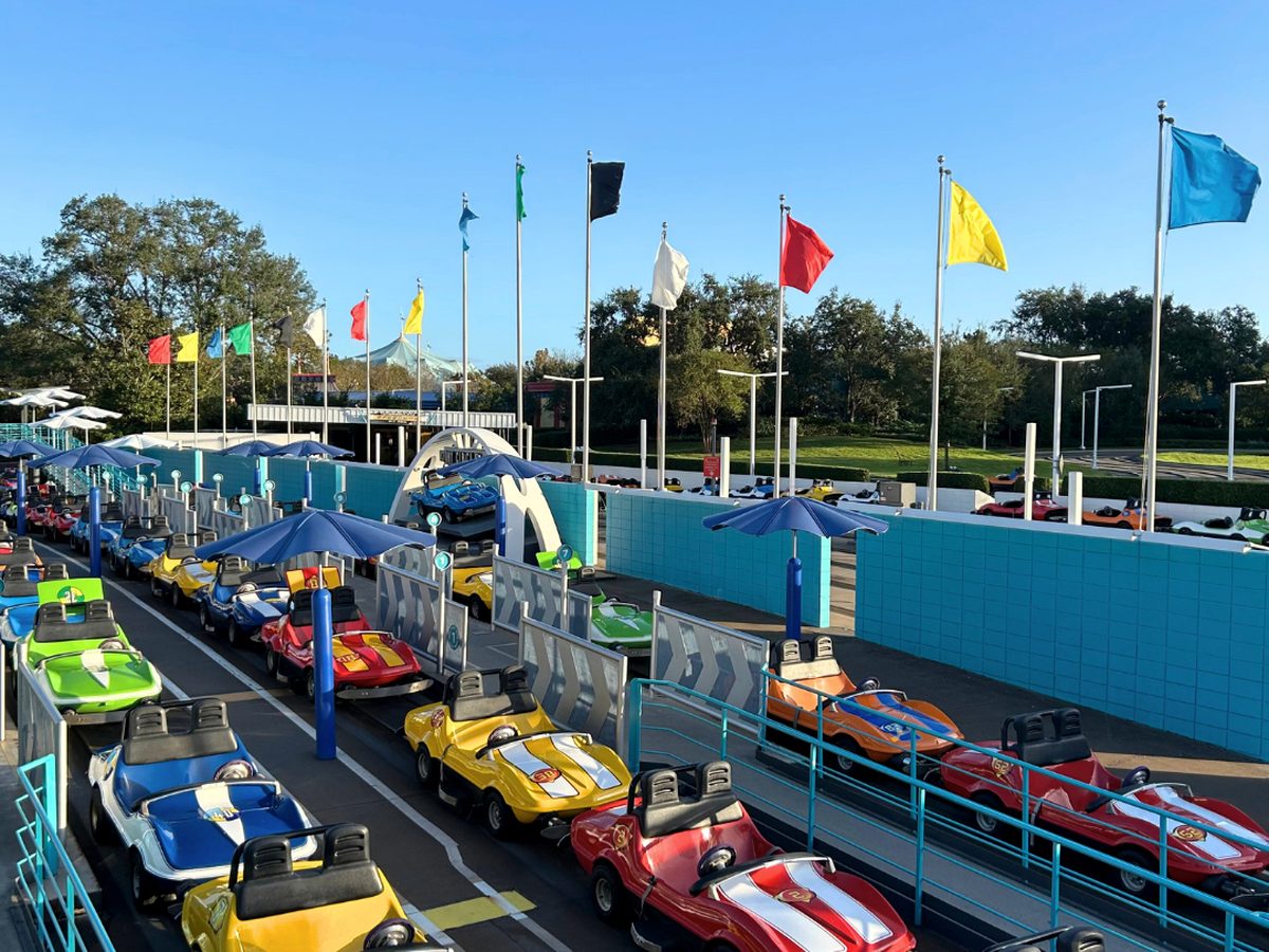 Rows of red, yellow, green and blue Tomorrowland Speedway go-karts on the track at Magic Kingdom, race flags flying behind