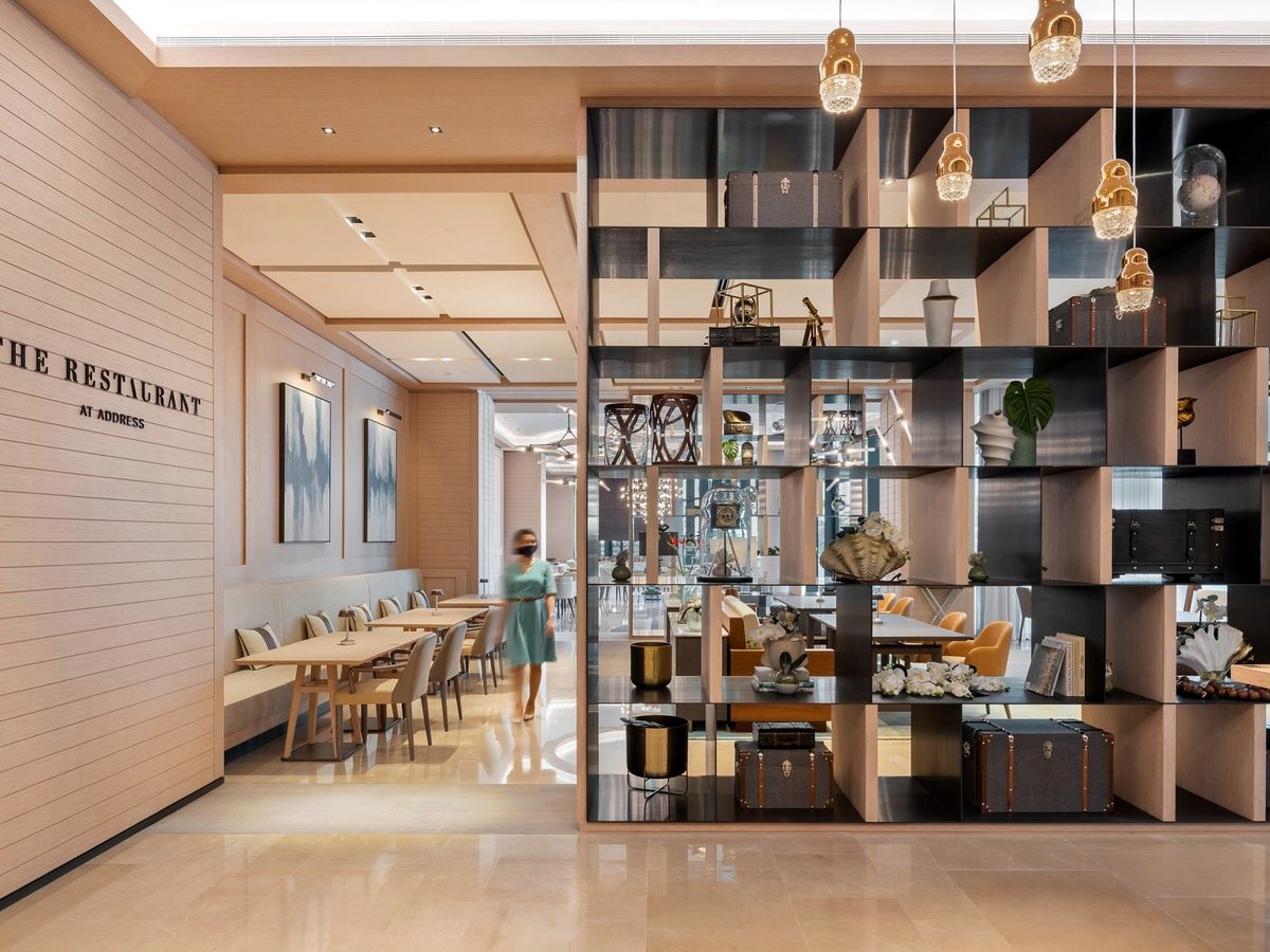 The entrance to The Restaurant, its name lettered on a pale timber wall beside a tall black display shelf of curios that screens the dining room.
