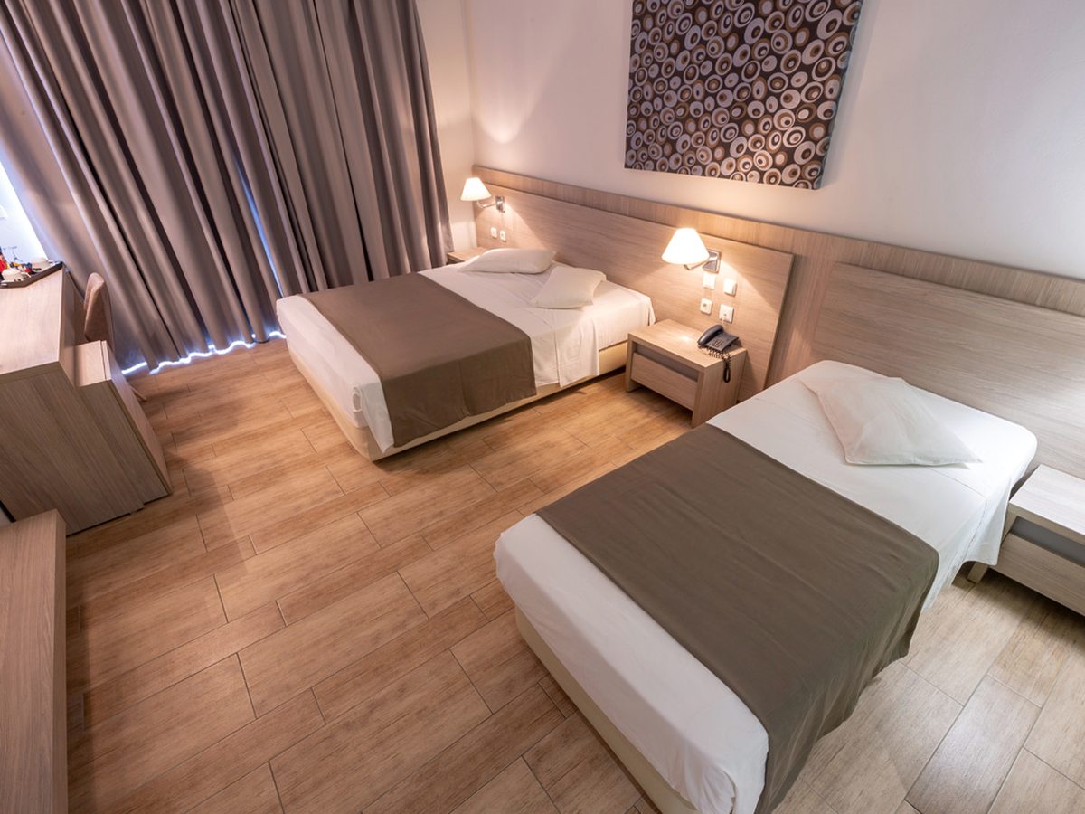 A guest room with a double bed and a separate single bed, a wood-effect floor, bedside reading lights and a desk.