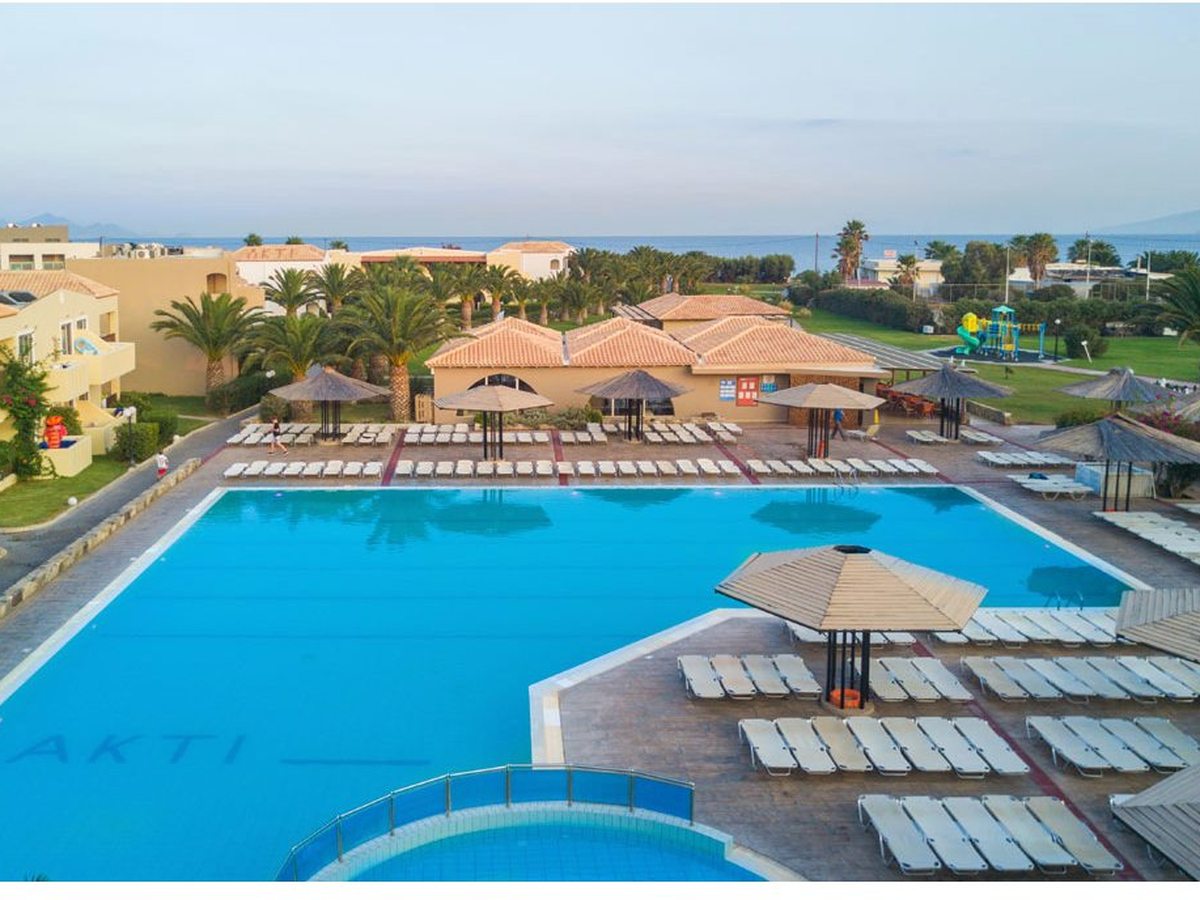 A large pool with the resort's name tiled into the floor, rows of sun loungers and thatched umbrellas and the sea beyond.