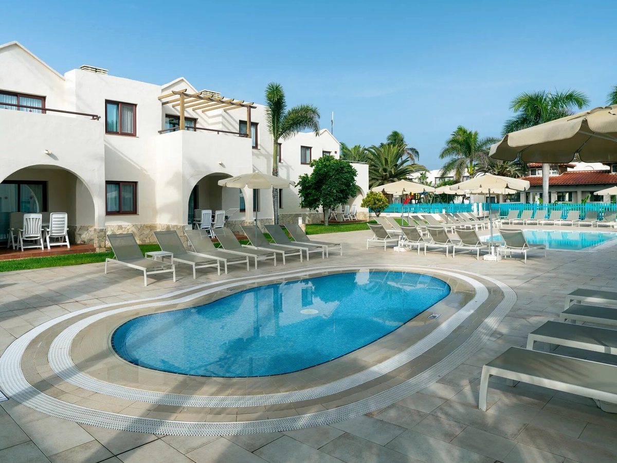 A small oval pool with a tiled surround and loungers, with whitewashed suite buildings and a larger pool behind.
