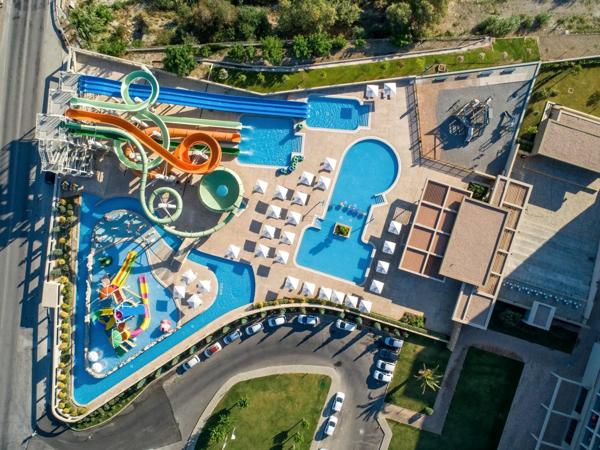 An aerial view of the waterpark, with blue, green and orange flume slides, a lazy river, pools and a colourful children's splash structure.