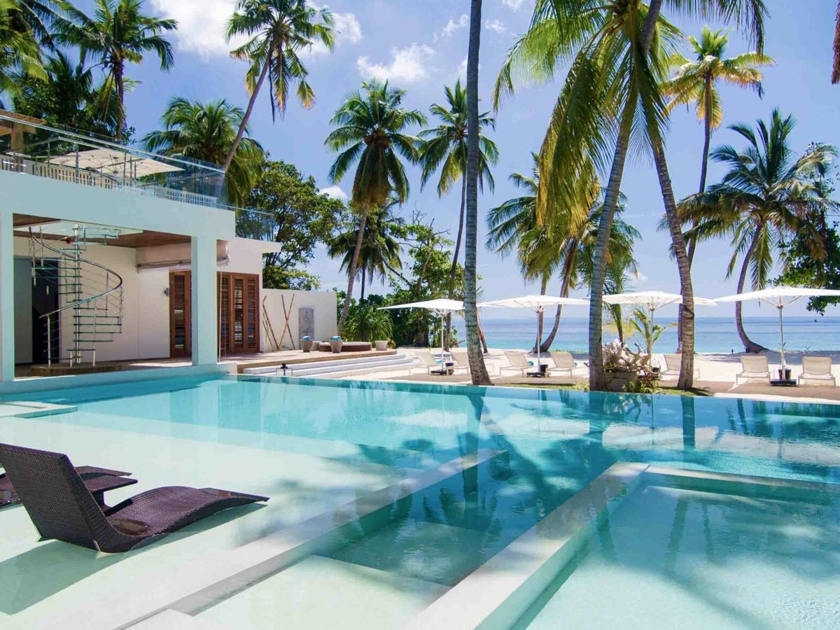 A large private pool with submerged loungers and steps, a two-storey Beach Residence with a glass spiral staircase behind and the beach beyond.