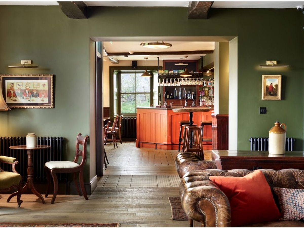 A green-walled pub lounge with traditional armchairs, framed pictures and a bar lined with bottles.