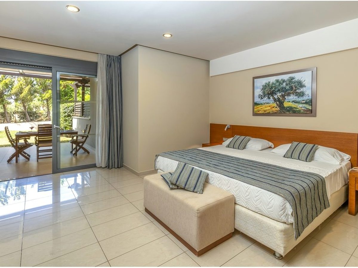 A ground-floor room with twin beds pushed together and sliding doors onto a covered terrace with a table and chairs beside the garden.