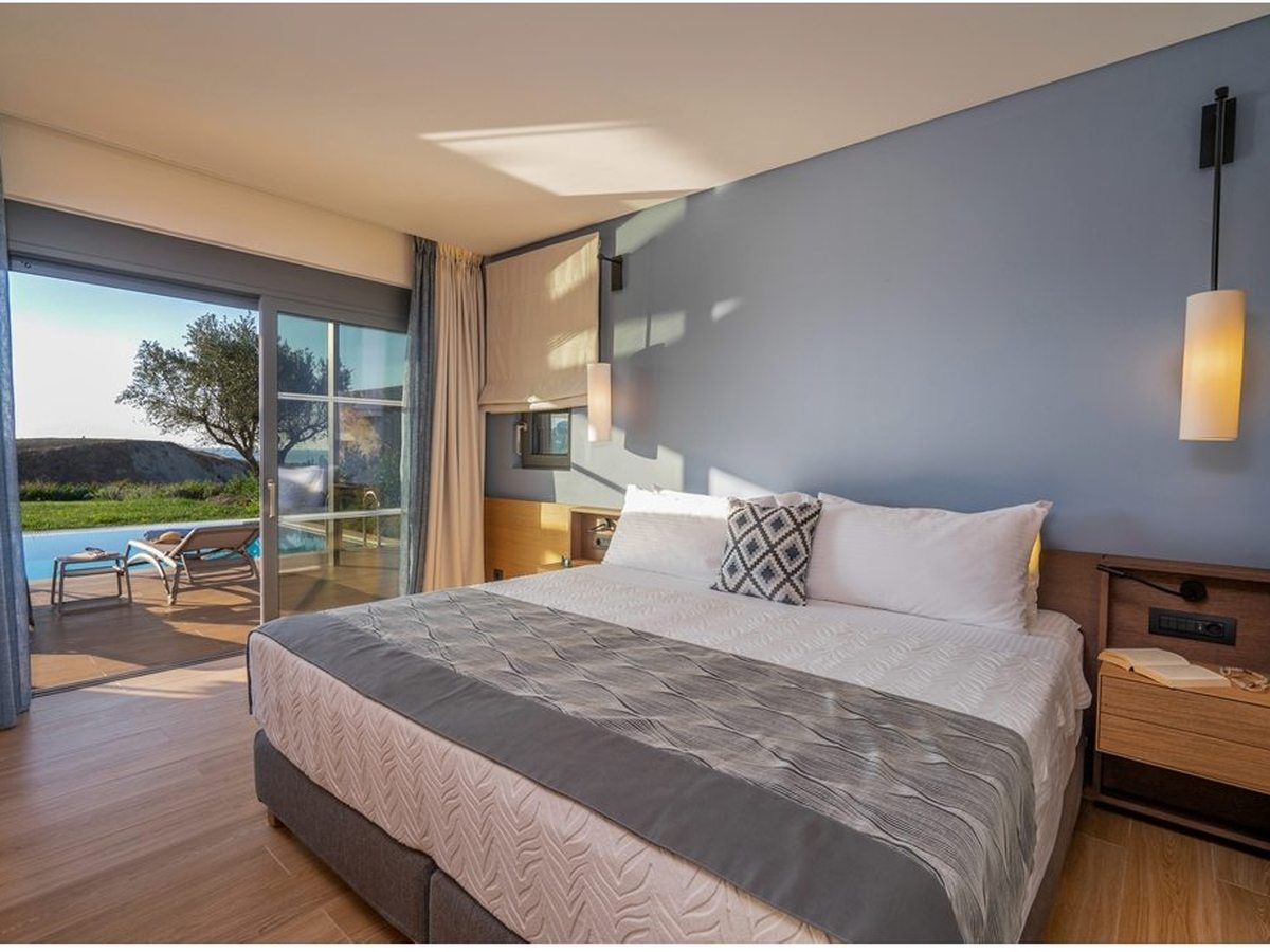 A contemporary room with a blue feature wall and wood-effect floor, sliding doors onto a terrace with sun loungers beside a private pool.