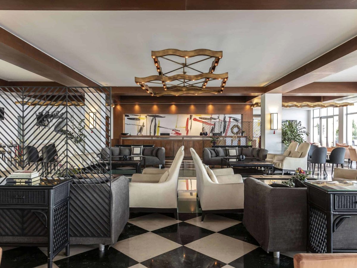 An indoor lounge bar with low sofas and armchairs, a patterned tiled floor and a decorative ceiling light.