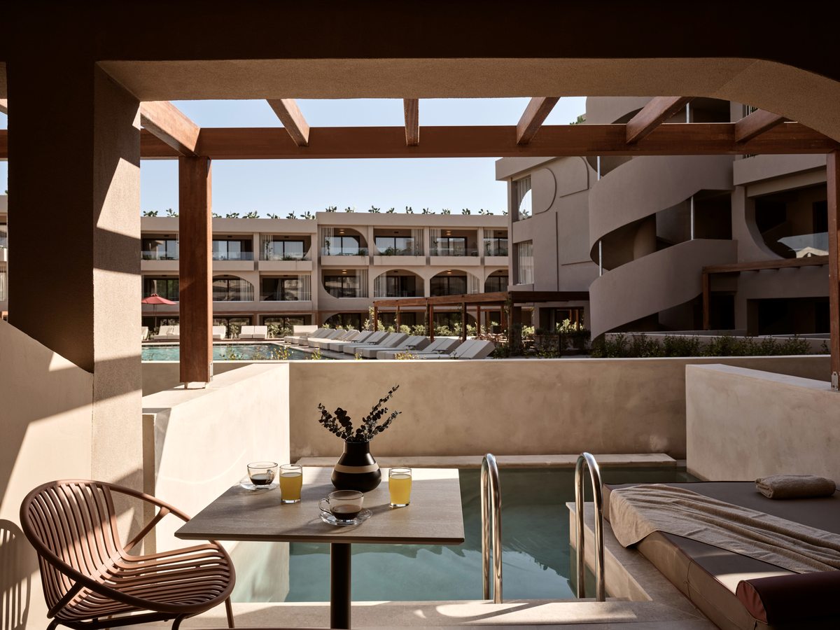 A shaded room terrace with its own small plunge pool reached by steps and a handrail, a daybed and a table set with coffee, looking out to the pool and room blocks beyond.