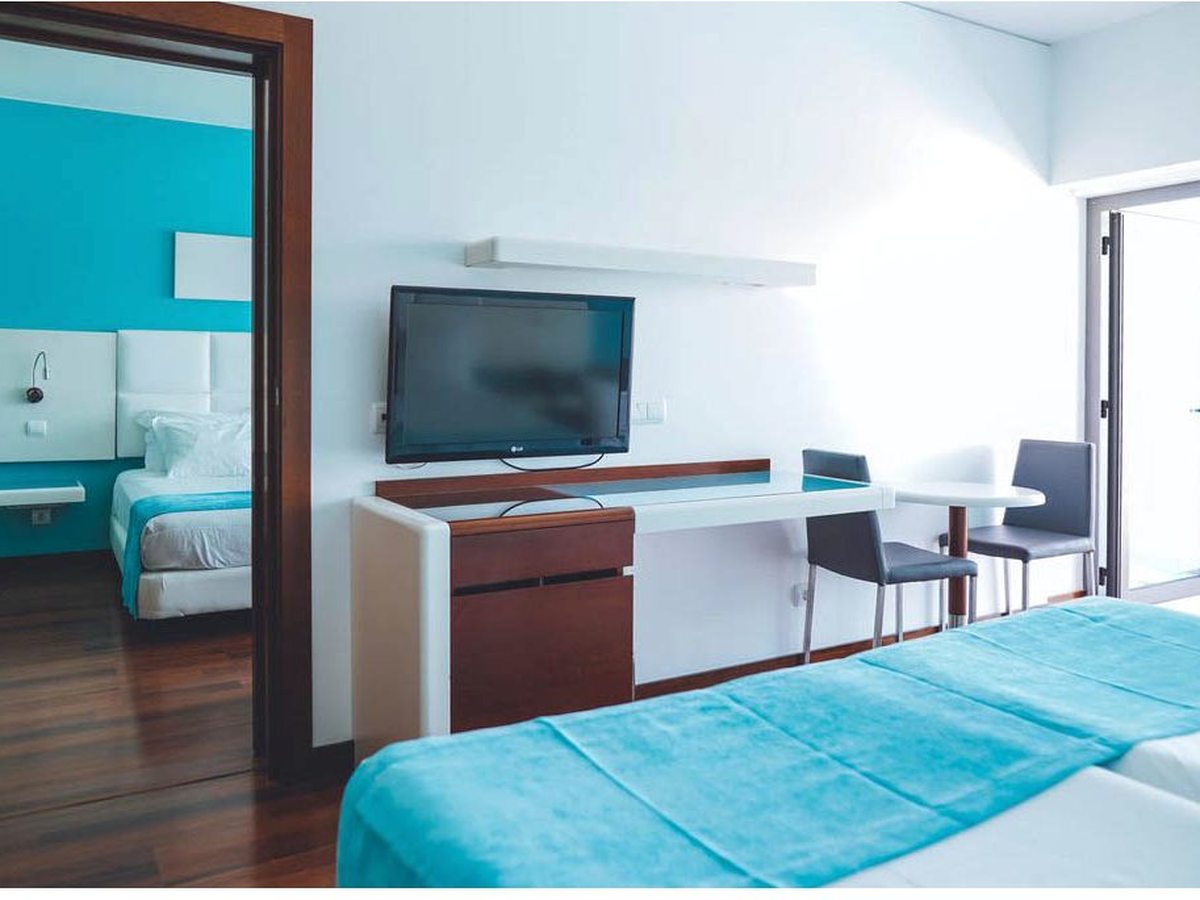 A twin room with a wall-mounted TV, a table and chairs and an open connecting door through to a second bedroom.