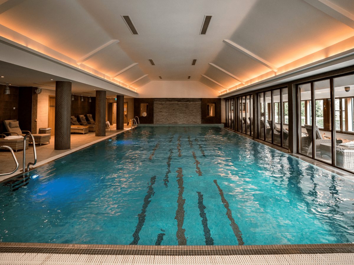 A long indoor pool with lane markings, warm cove lighting and a glazed wall onto the garden.