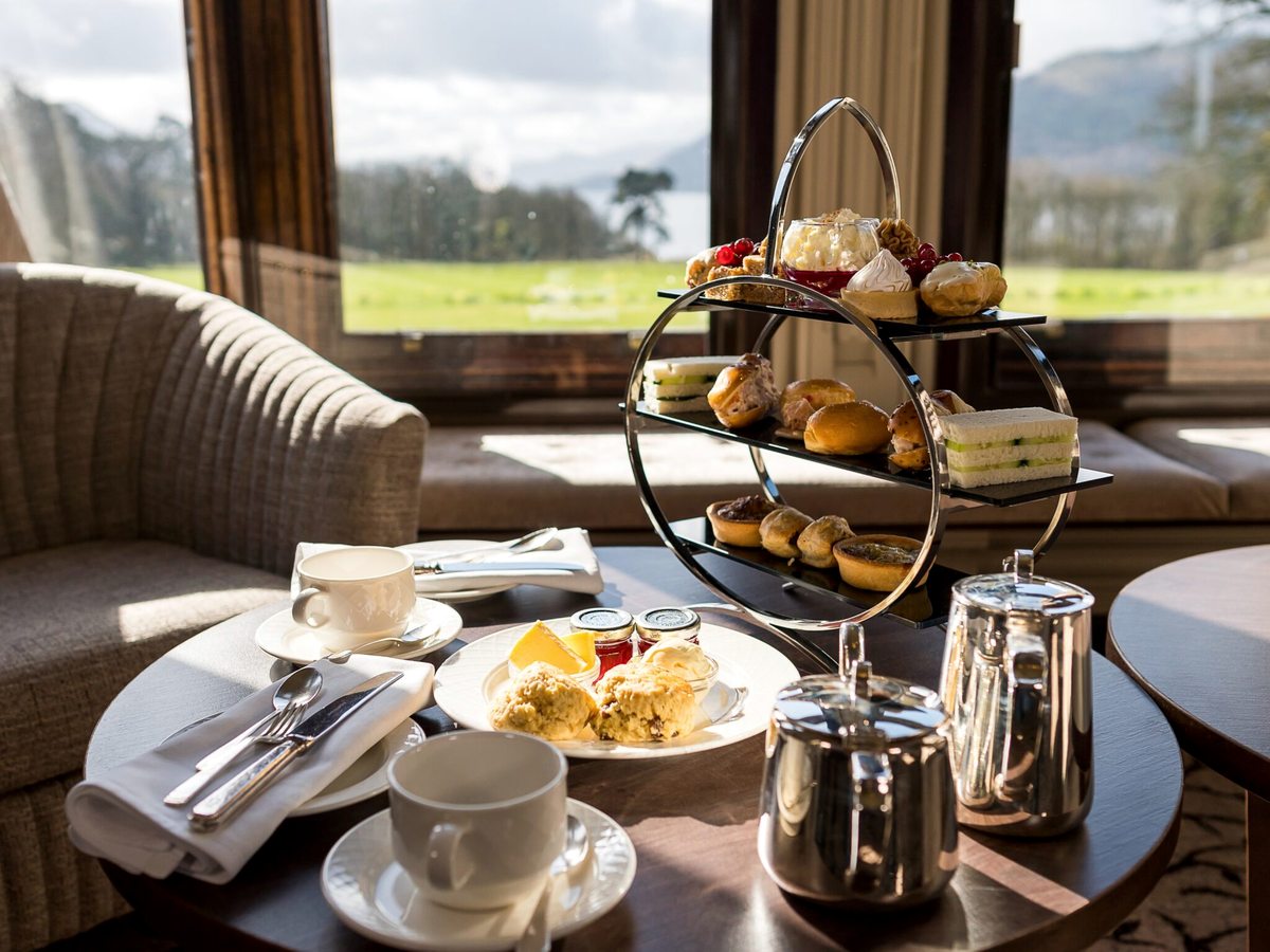A tiered afternoon tea stand of sandwiches and cakes on a table by a window with a country view.