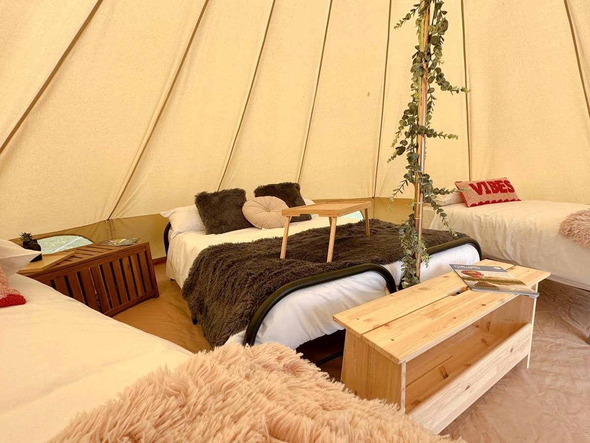 A festival-styled bell tent interior with two made-up beds, cushions and throws and a wooden storage chest on a rug-covered floor.