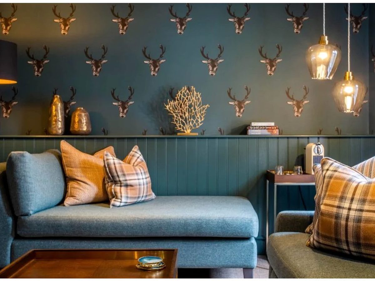A separate suite lounge with a teal day-bed and armchair against teal stag-motif wallpaper and green panelling, with a coffee machine on a side table.
