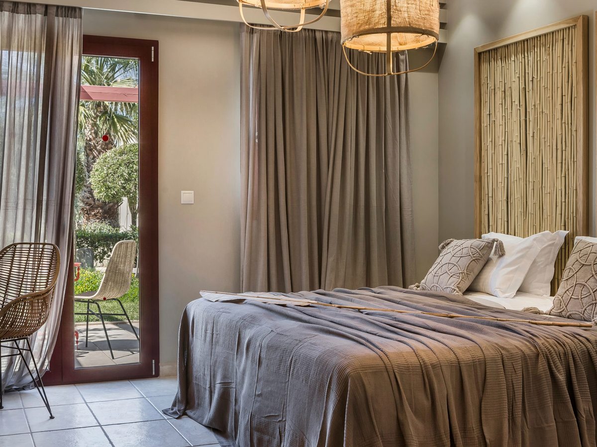 Ground-floor double room with a woven headboard and glass doors opening straight onto a garden terrace and lawn.