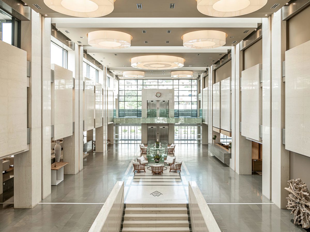 A double-height atrium lobby with a circular skylight, a glazed entrance wall and a long polished floor.