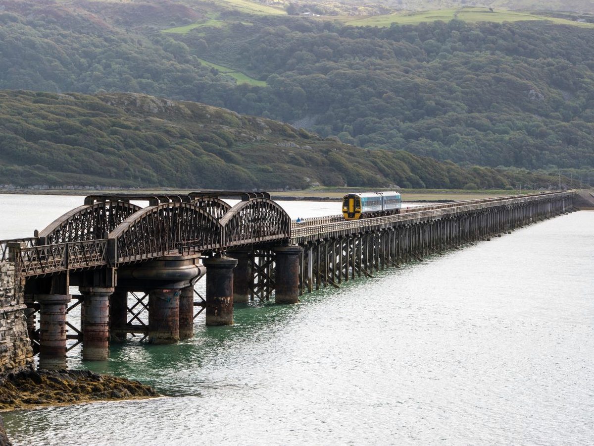 A long low railway viaduct crossing a wide tidal estuary, with wooded hills beyond.