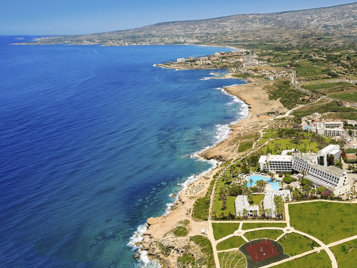 Aerial view of the resort's low white buildings and gardens along a rocky Mediterranean coastline.