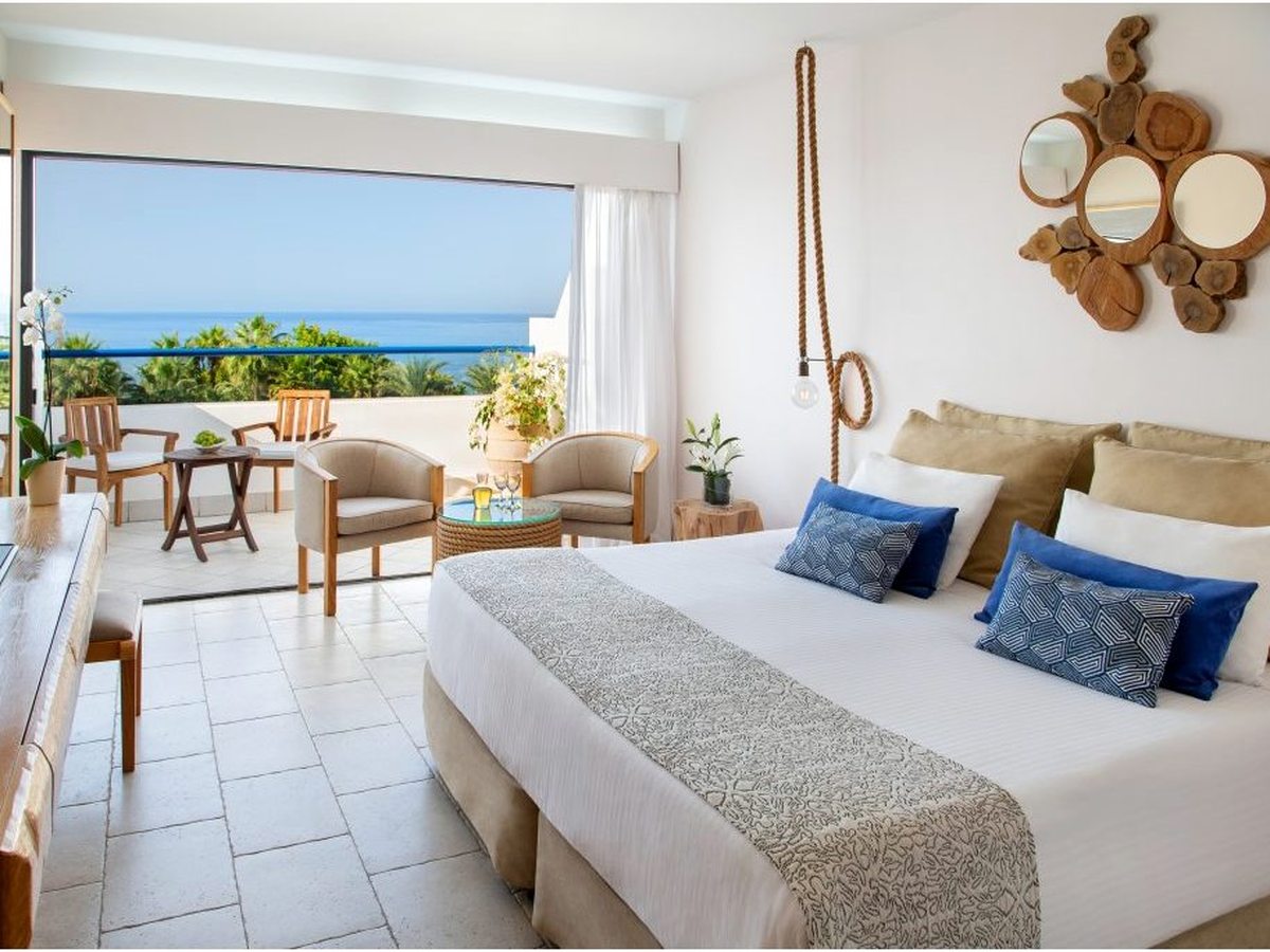 A bright room with a double bed and balcony doors open to a sea view.