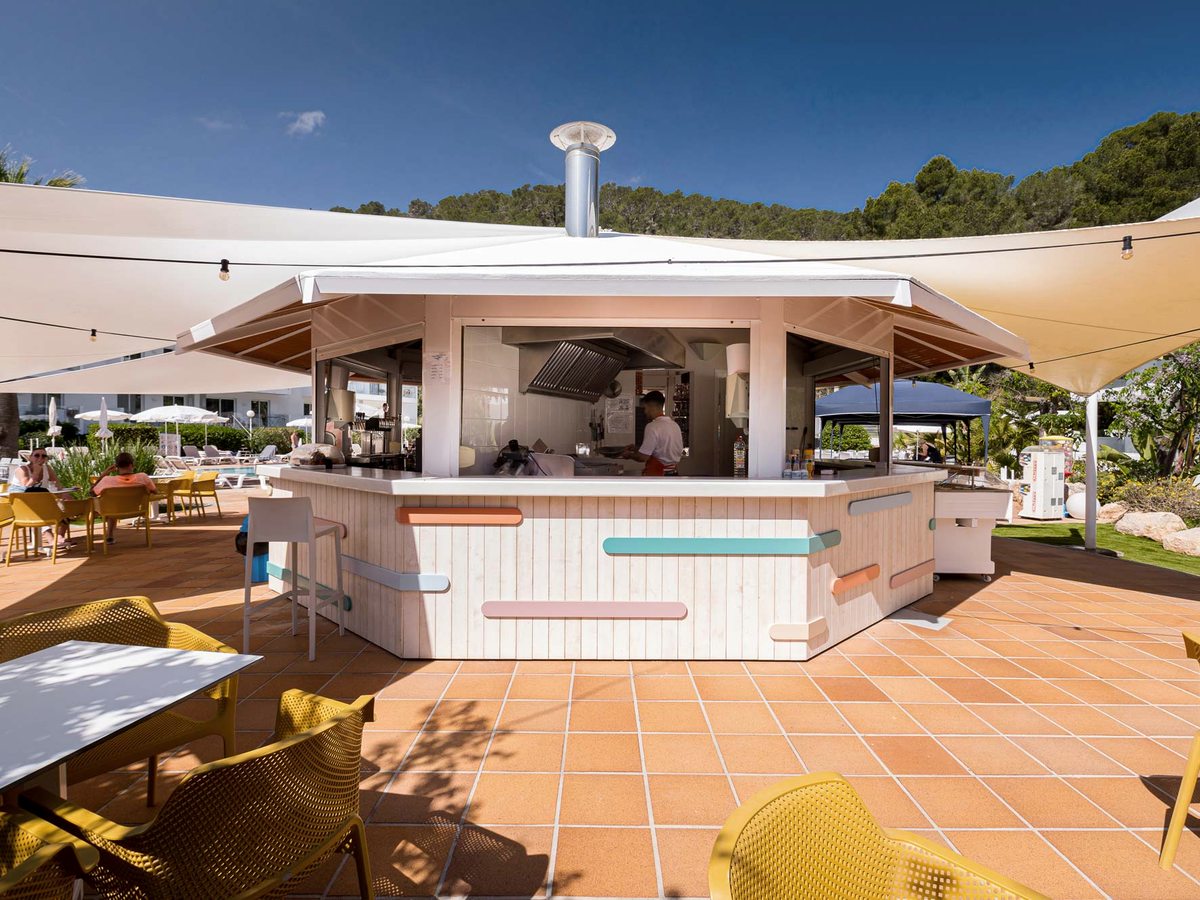 Free-standing poolside kiosk bar with a pastel-panelled wraparound counter, bar stools and a tiled terrace.