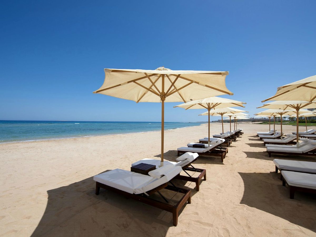 A sandy beach lined with wooden sun loungers under cream parasols beside the calm turquoise Red Sea.